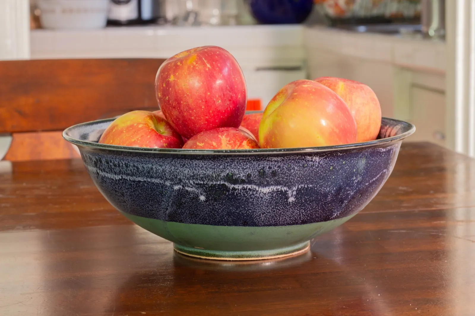 The bowl holding apples on the kitchen table, a chair drawn up beside it.