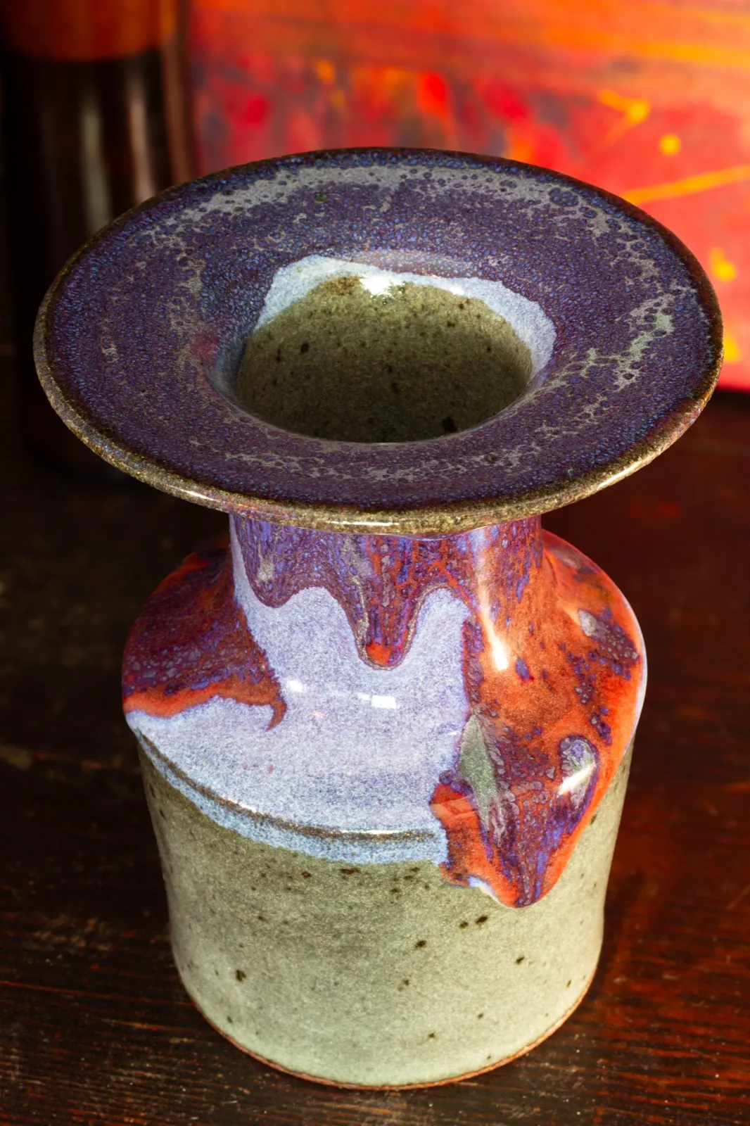 A stoneware bottle with a wide flat purple rim, red and purple glaze flowing down its neck onto a speckled oatmeal body.