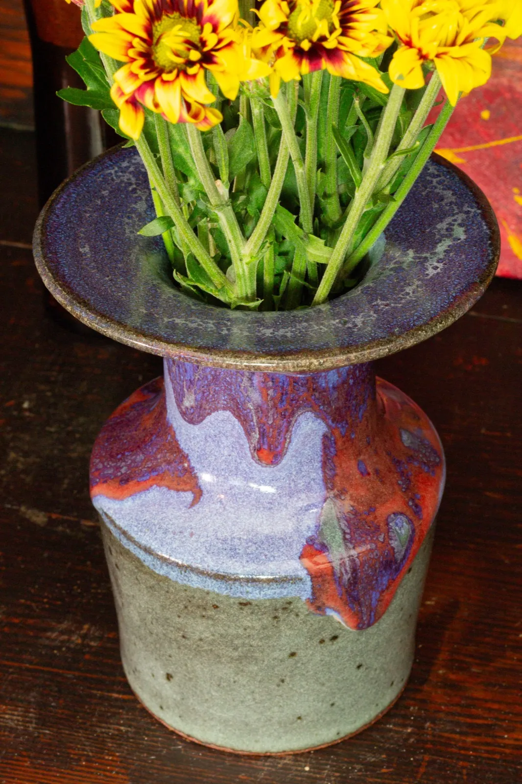 The bottle seen from above the rim, flowers rising out of it, the purple flange catching the light.